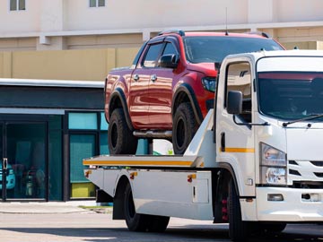 Ein rotes Pickup wird in einer sonnigen städtischen Umgebung auf einen weißen Abschleppwagen von Unfallwagenankauf Ahaus verladen.